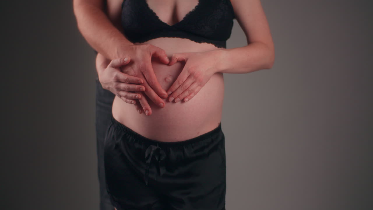 пара родителей кладет руки в форме сердца на живот беременной женщины.