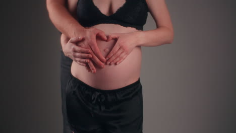 pareja de padres colocando sus manos en forma de corazón en el vientre de una mujer embarazada