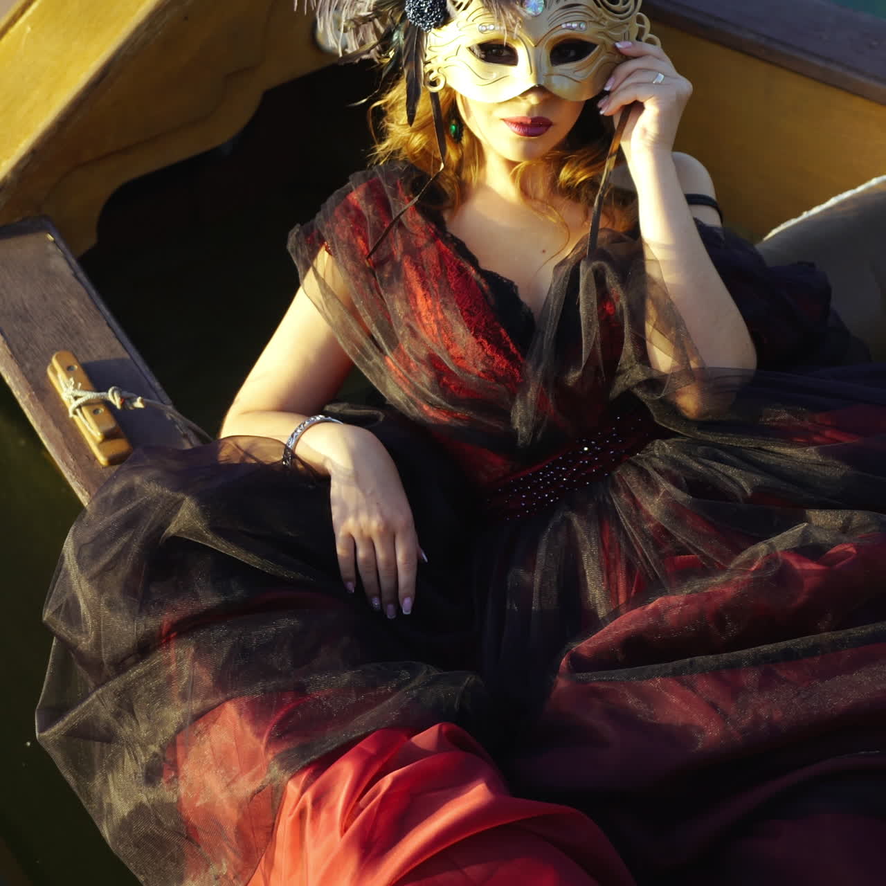 Sexy woman dressed in traditional costume in Venice during the carnival sitting in the gondola. Elegant and mysterious lady in mask admires nature on the river background.