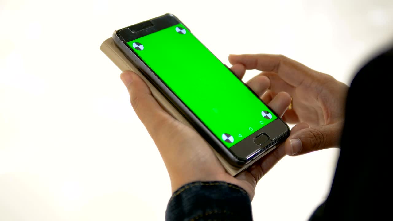 Hands of woman holding smartphone with green screen and tracking mark