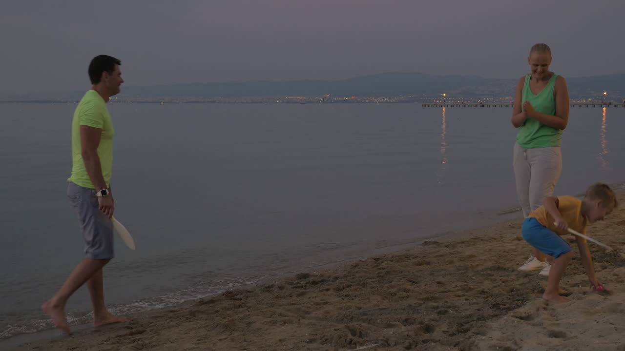 родители и сын играют в теннис на пляже.