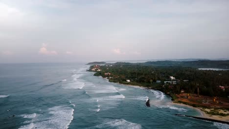 aerial birds eye view of beautiful foaming sea waves breaking near tropical shore with green trees and construction site