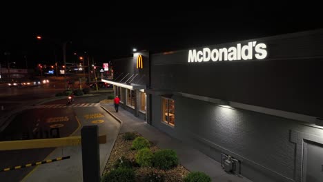 person walking on sidewalk of mc donalds restaurant at night. famous fast food building in usa. motorbike entering drive thru line. aerial establishing shot.