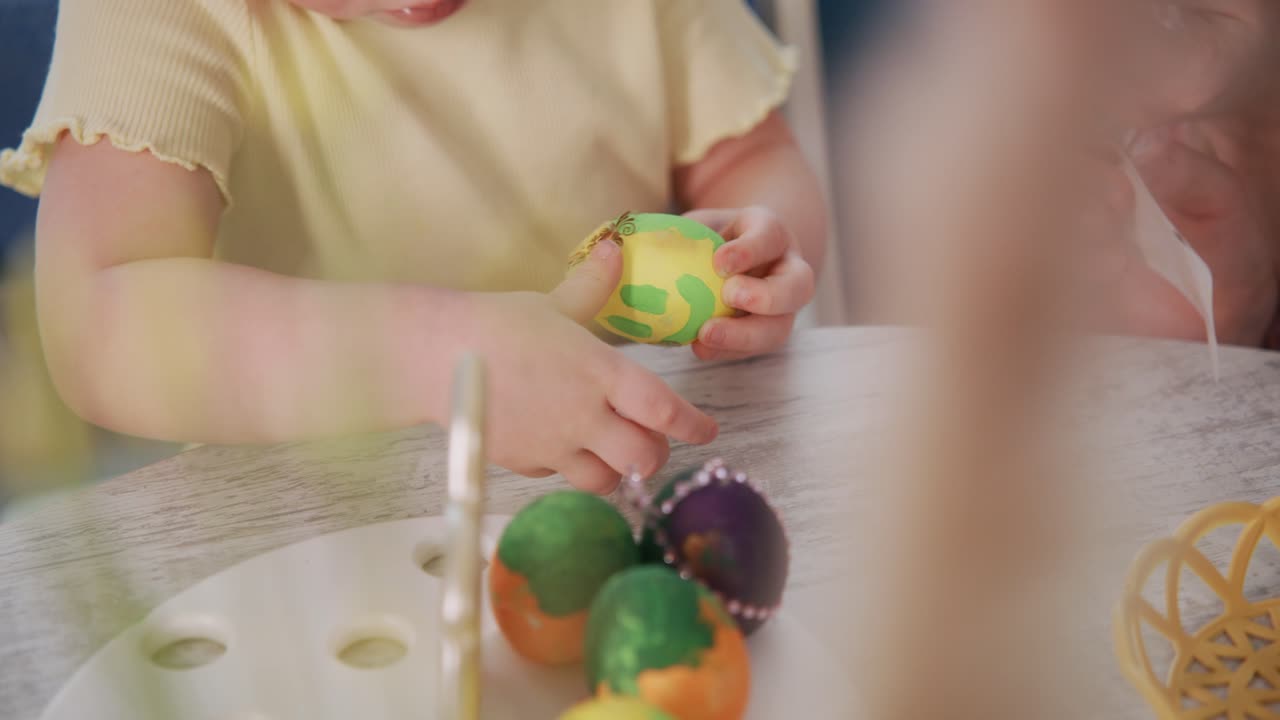 Ein Kind bemalt behutsam farbenfrohe Ostereier mit voller Konzentration. Kleine Hände tragen sorgfältig Farbe auf, während es an einem weißen Tisch sitzt. Leuchtend bunte Eier liegen in der Nähe, bereit zum Verzieren.