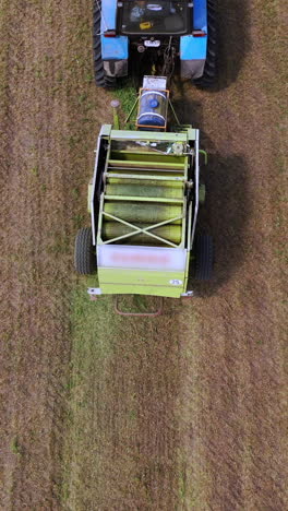 ready grass bale comes out of a pressing machine. agricultural machinery presses grass to make round bundle in the field. top view. vertical video