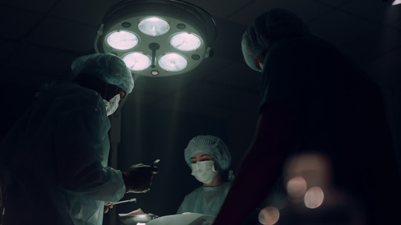 un equipo de cirujanos operando en una sala estéril oscura, trabajadores médicos salvando a un paciente.