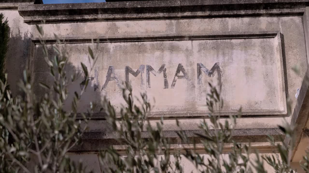 Inscription on historical stones of the word &amp;quot;Hammam&amp;quot;, in the foreground an olive tree