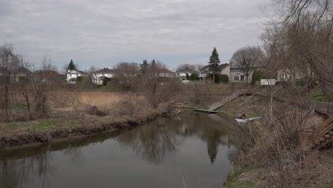 we see a beautiful river with reflections on the water, adding a lovely dimension on a slightly cloudy day. many leafless trees mark the beginning of spring.