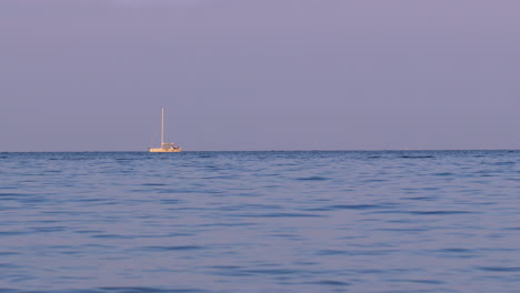 wide seascape at golden hour with a lone sailboat on the horizon under pastel violet sky; tranquil maritime panorama