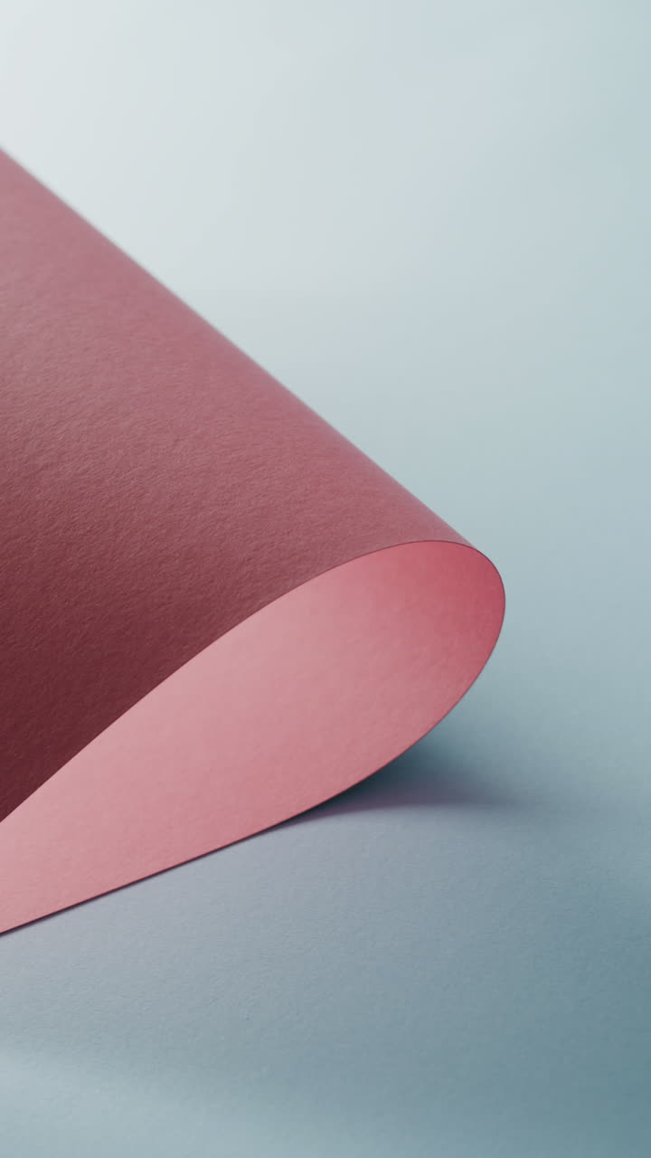 Vertical video of close up of pink rolled piece of paper on blue background with copy space