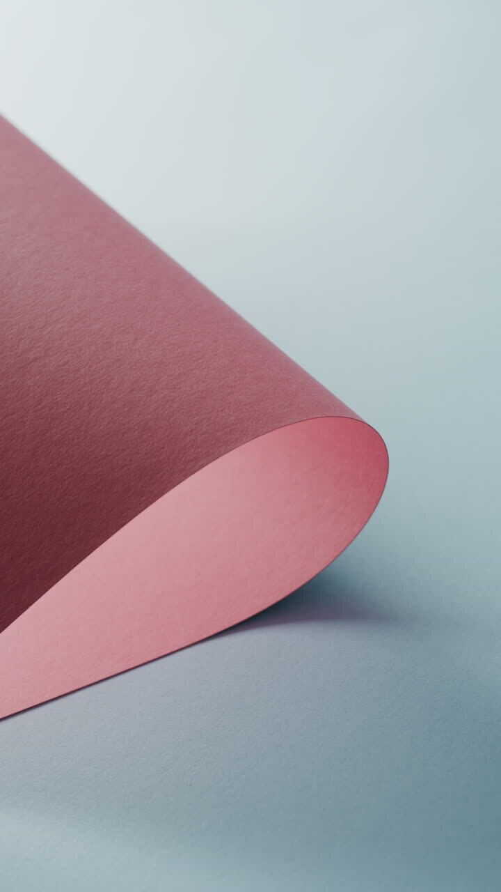 Vertical video of close up of pink rolled piece of paper on blue background with copy space