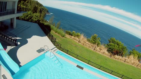 FPV-Drone-shot-of-a-luxurious-private-resort-on-the-edge-of-a-cliff-surrounded-by-lush-green-foliage