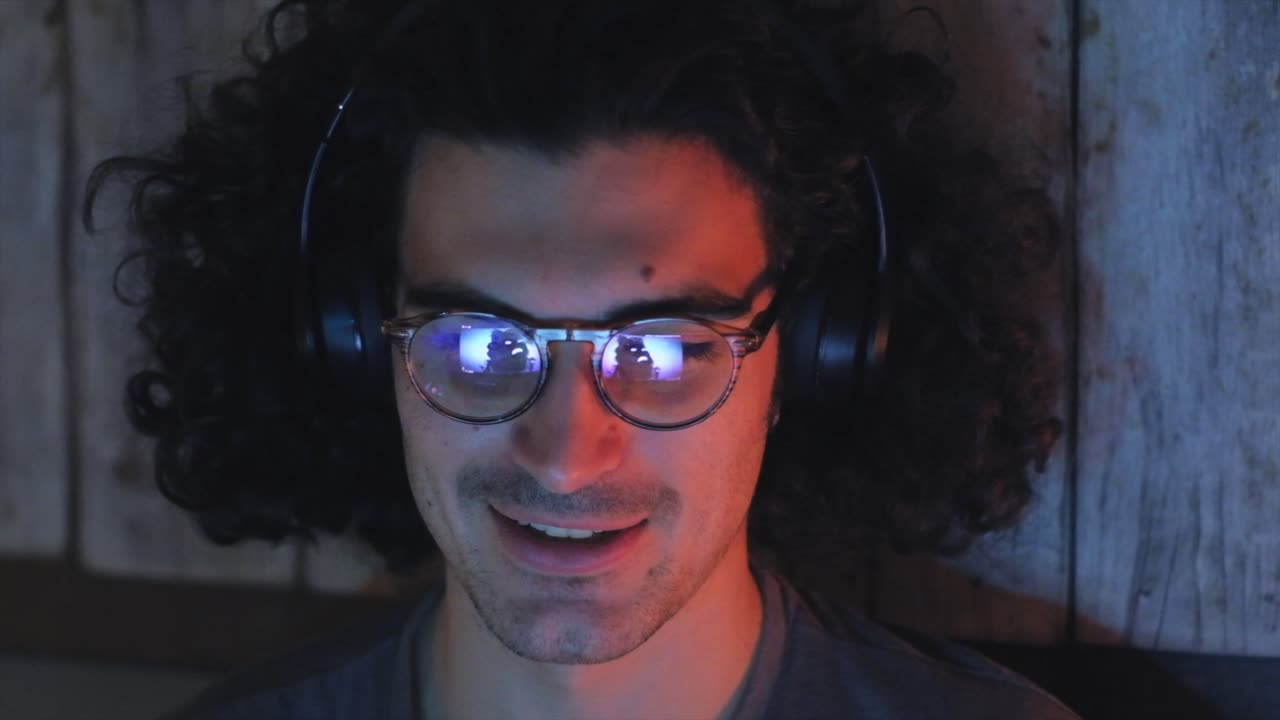 hombre de cabello rizado con auriculares y gafas disfrutando de música en la computadora portátil