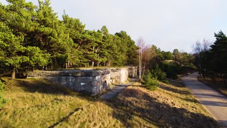 Aerial-view-of-concrete-Northern-fortification-ruins-covered-by-green-vegetation-and-trees-located-in-Liepaja,-Latvia-in-sunny-day,-wide-angle-establishing-drone-shot-moving-forward