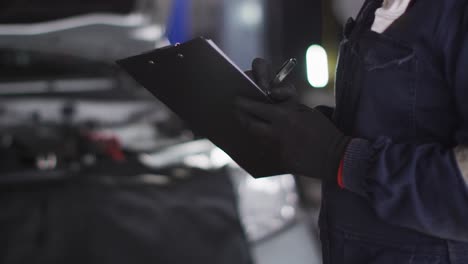 sección media de la mecánica femenina tomando notas en el clipboard en una estación de servicio de coches