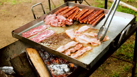 freír tocino y salchichas en una sartén de acero inoxidable a fuego abierto - desayuno de campamento