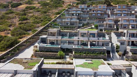 view of cayoresort in greece crete - brunette haired woman in bathing suit sitting by pool and drinking cocktail - drone flying backwards fast