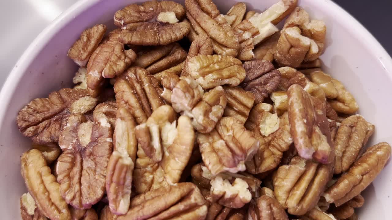 Overhead shot of pecan halves filling a small bowl, creating a textured background ideal for food photography, healthy eating concepts, or recipe illustrations, top down panning shot