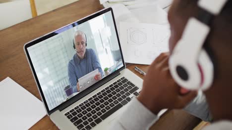 African-american-businessman-sitting-at-desk-using-laptop-having-video-call-with-male-colleague