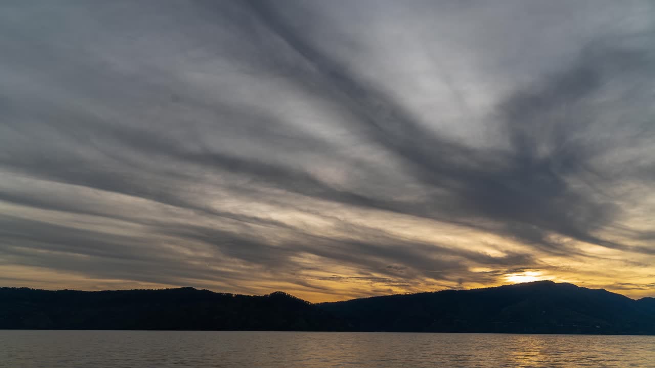 Dramatic Sunset Over Lake with Silhouetted Mountains and Cloud Streaks