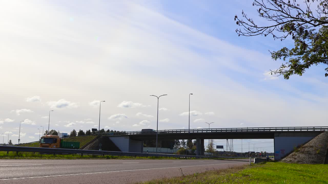 Time lapse or timelapse footage of Pärnu highway and a bridge over and underpass during summer time when its slightly cloudy and sunny. Cars and vehicles driving, speeding on the road with markings.