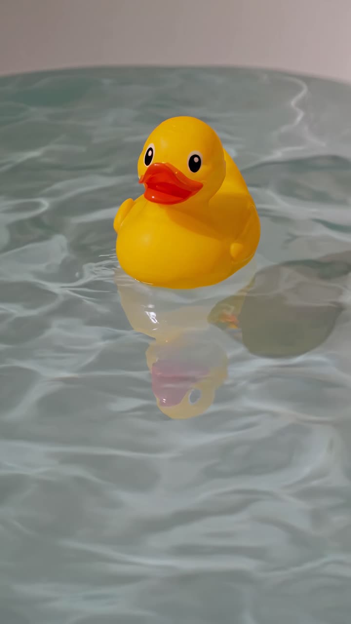 A close-up video of a yellow rubber duck floating on rippling water, captured from a low angle