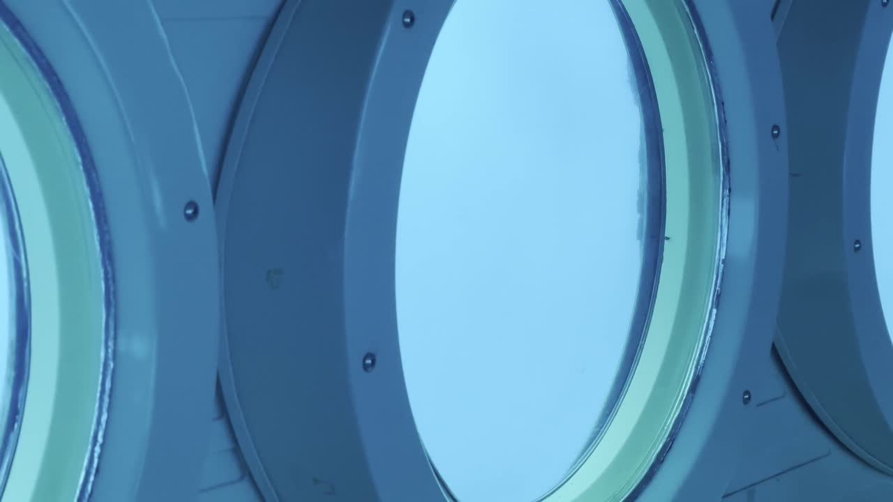 Cinematic panning shot along a row of portholes inside a submarine below the surface of the ocean off the coast of Hawai'i