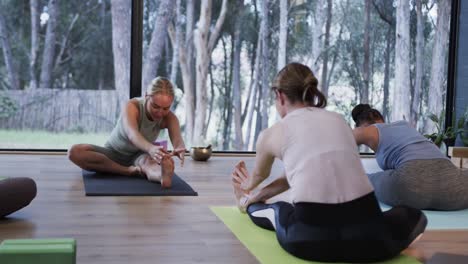 Focused-diverse-women-stretching-together-on-mats-in-yoga-class-with-female-coach,-slow-motion