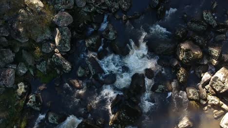 low flying aerial of river flowing over rocks