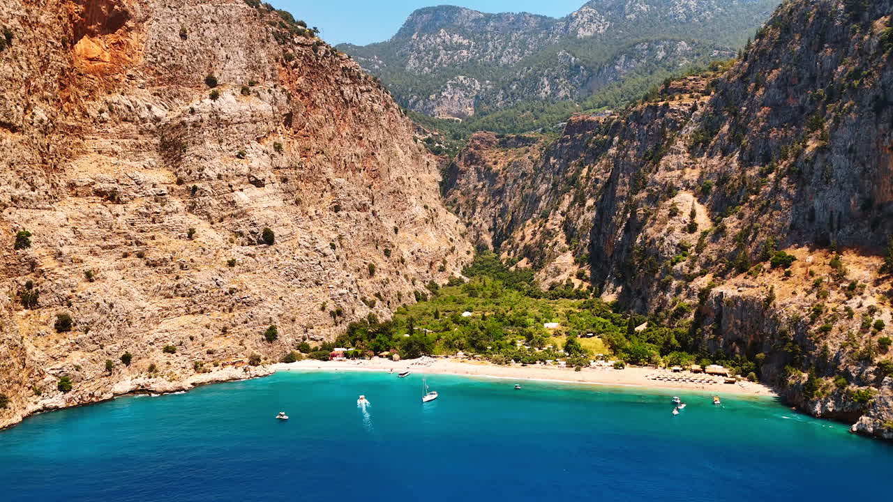 Scenic view of a tranquil bay in Turkey. Stunning cliffs rise above a serene turquoise bay, with boats gently gliding over calm waters beneath a clear sky