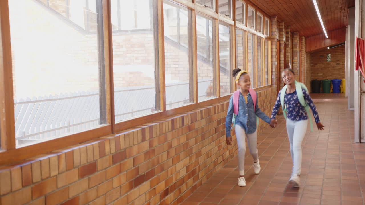 Walking in school hallway, two girls holding hands and smiling, copy space