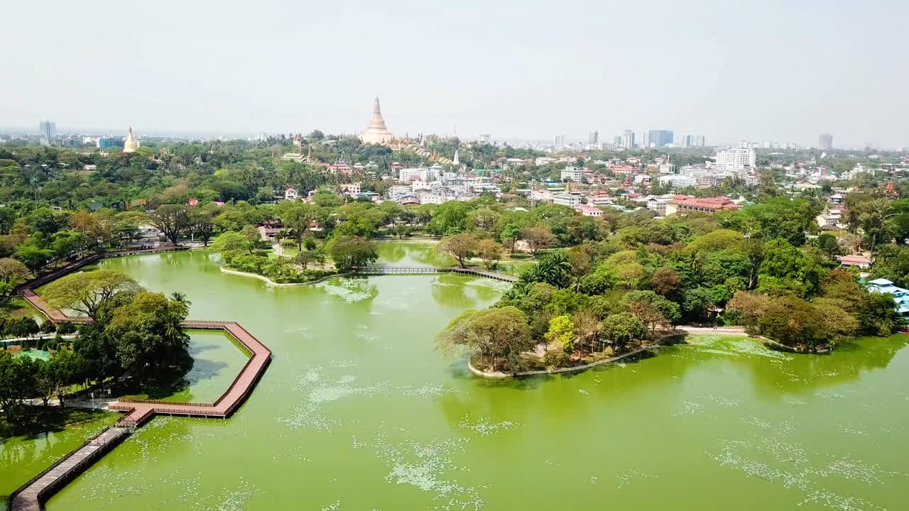 vista aérea del lago kandawgyi de rangun rodeado de exuberante vegetación, con la pagoda dorada de shwedagon en el fondo. una combinación serena de naturaleza, arquitectura y paisaje urbano