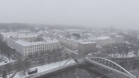 Tiro-De-Drone-Del-Puente-De-Arco-Peatonal-Sobre-El-Río-Emajõgi,-Ciudad-De-Tartu-Cubierta-De-Niebla