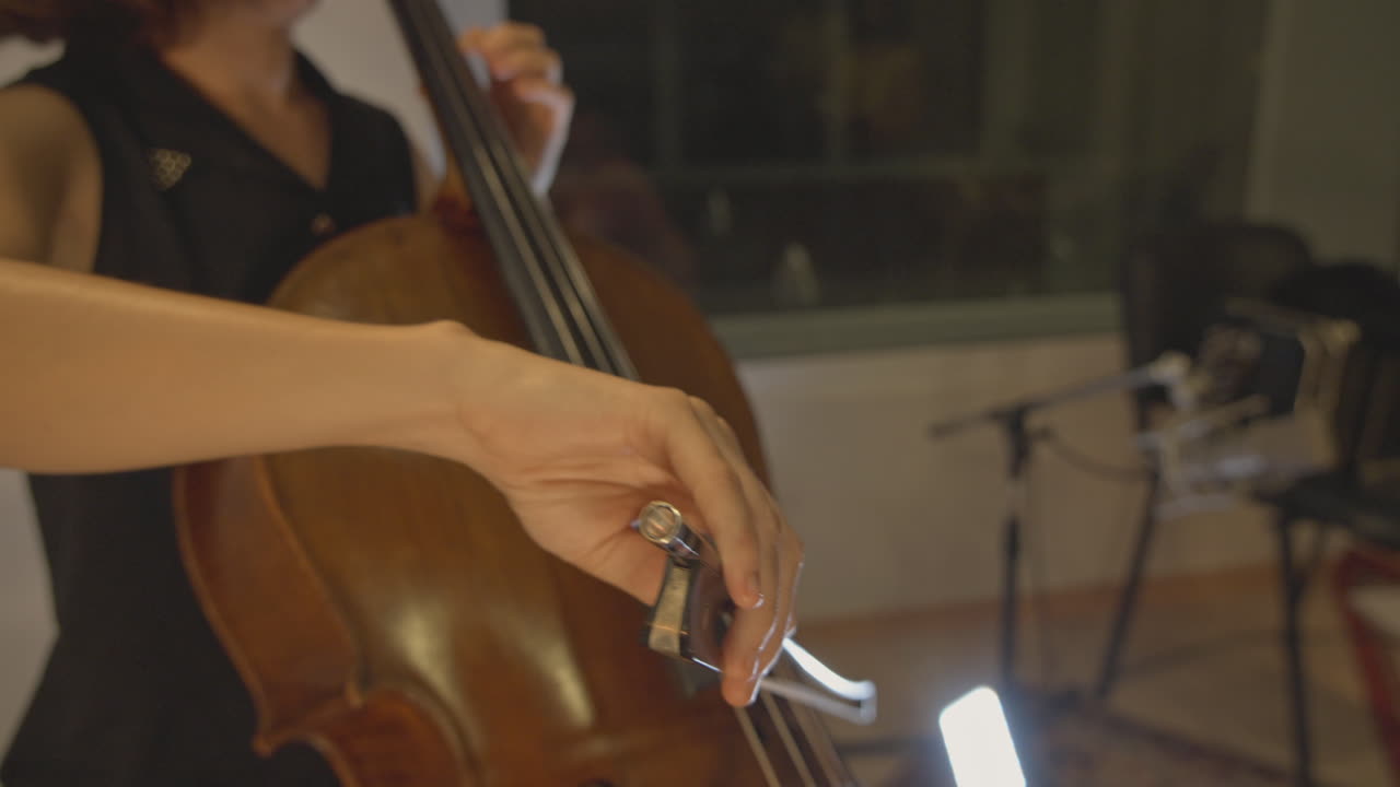 Primo piano di un musicista che suona il violoncello con l'archetto in studio.