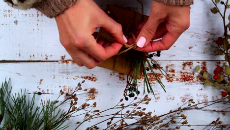 close-up of hands carefully tying a twine bow on a gift, adding natural pine and berry accents. rustic, festive wrapping scene perfect for holiday promotions, crafts, and seasonal content.