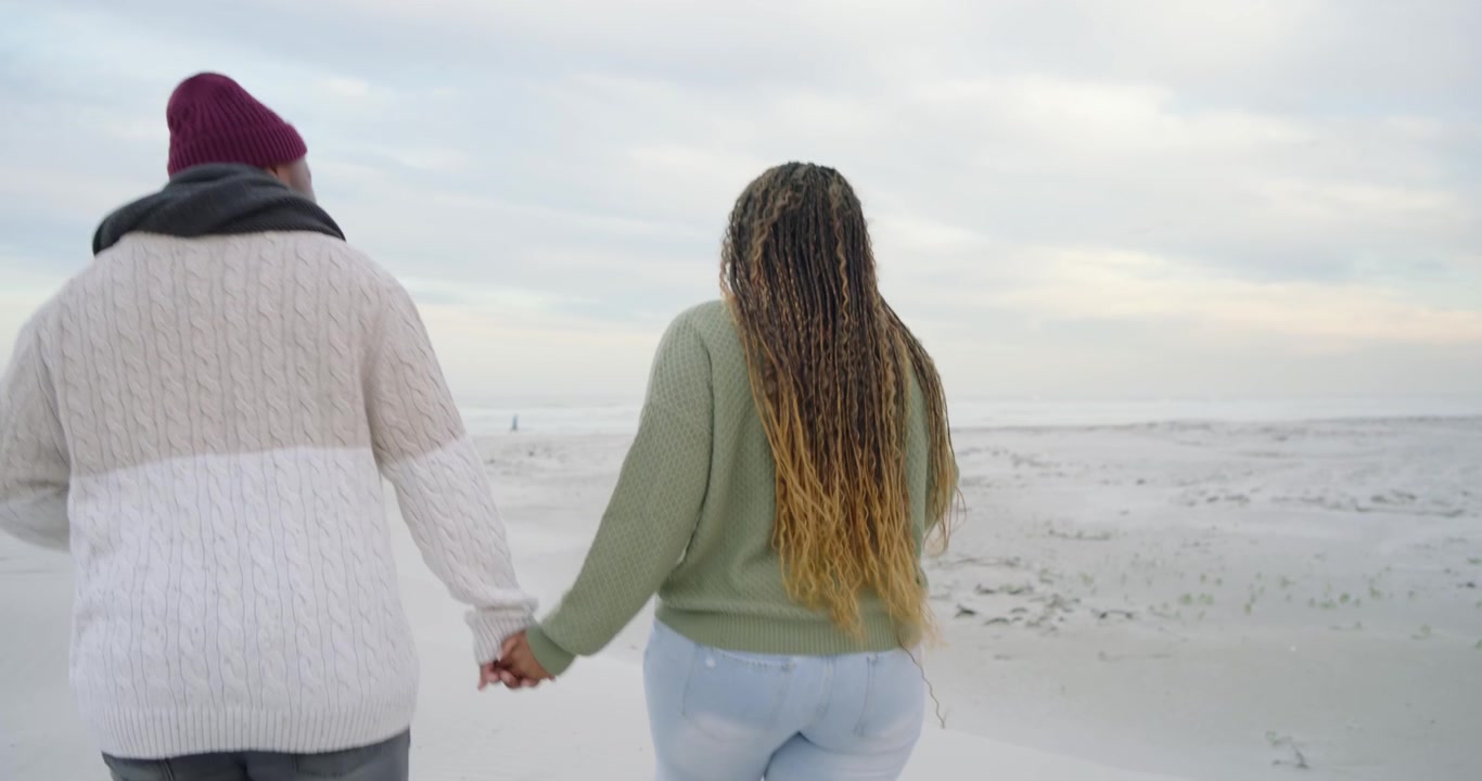 African American couple walking holding hands to horizon on beach after brief chat, man with scarf