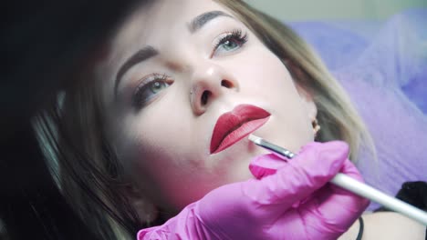 makeup procedure. lip brush stroke in a beauty salon. makeup master in pink rubber gloves