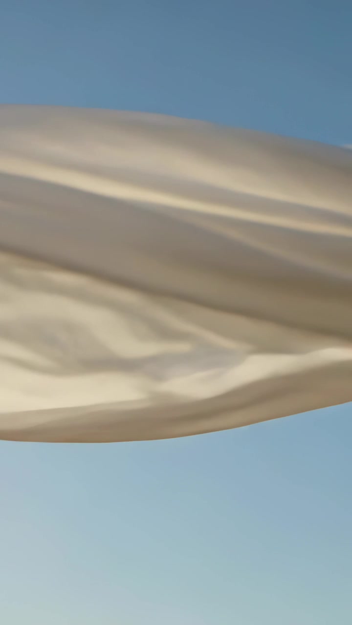 Vertical video: Billowing light fabric sweeping across open blue sky, wind causing rippling folds