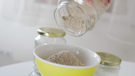 Slow-motion-close-shot-as-brown-almond-wheat-falling-into-a-bowl,-from-a-white-jar