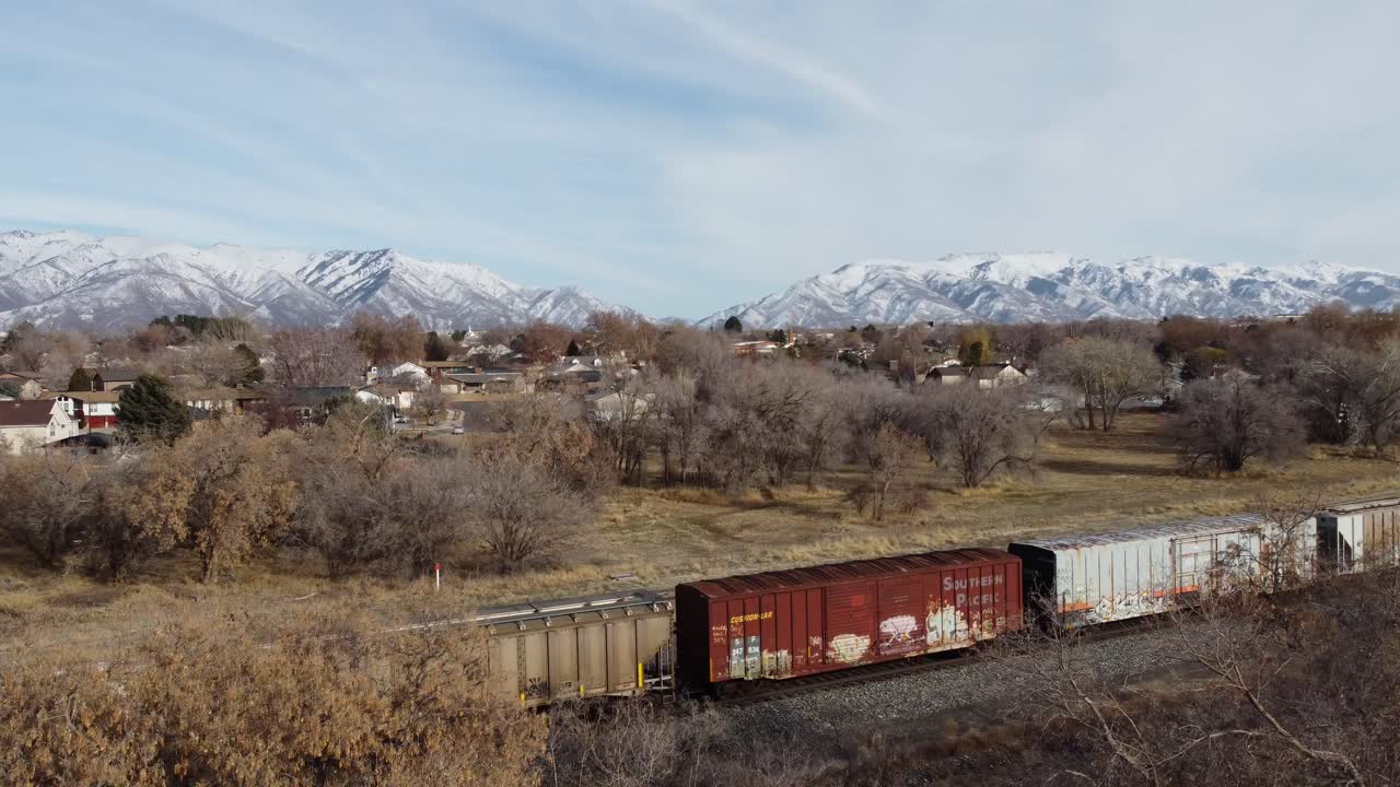 Drone clip flying through tree to view train rolling on railroad tracks, and panning around to see train end