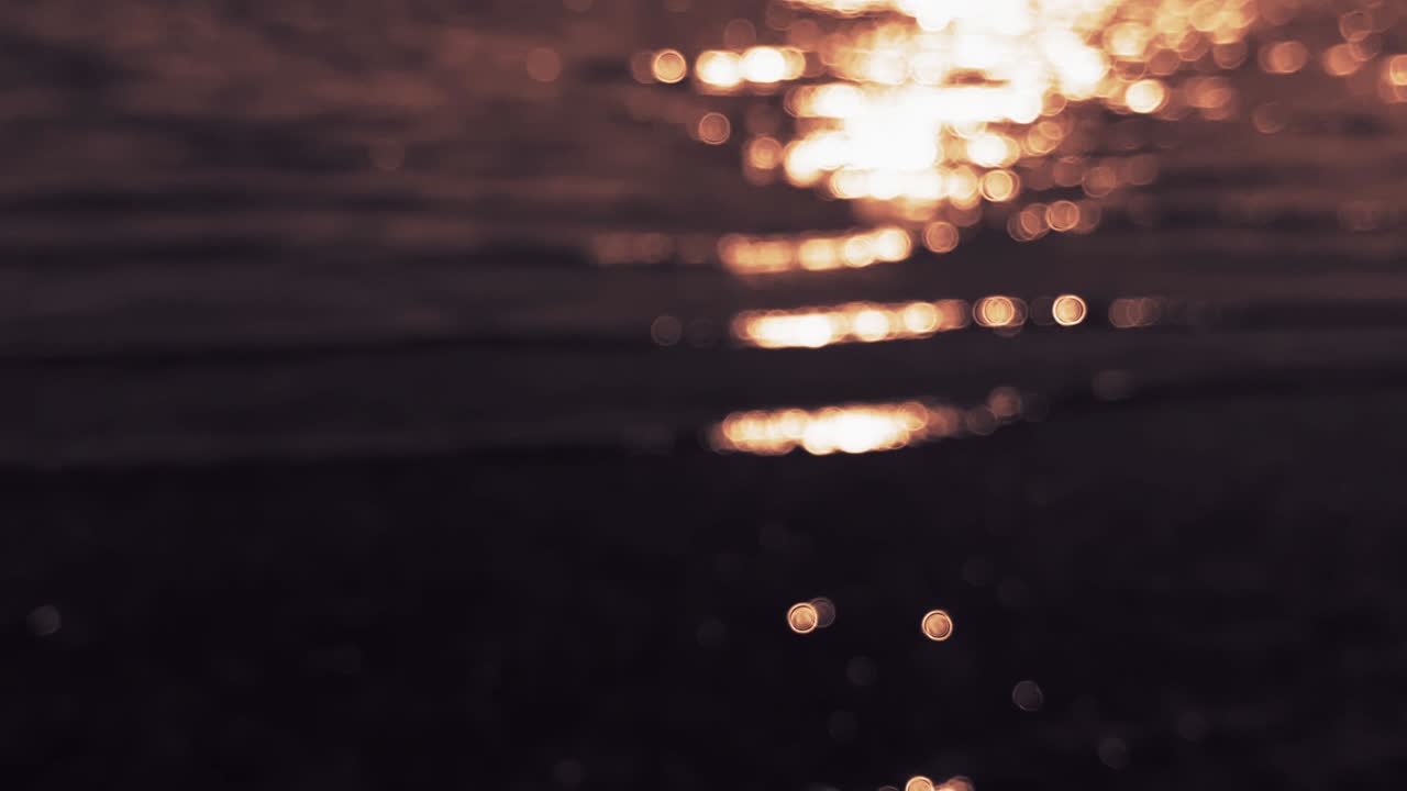 Defocused ripple of river in sun light, shining reflection on its surface. Blurred golden water surface at sunset, background. Abstract Blinking sea, river or ocean blurry backdrop. Bokeh.