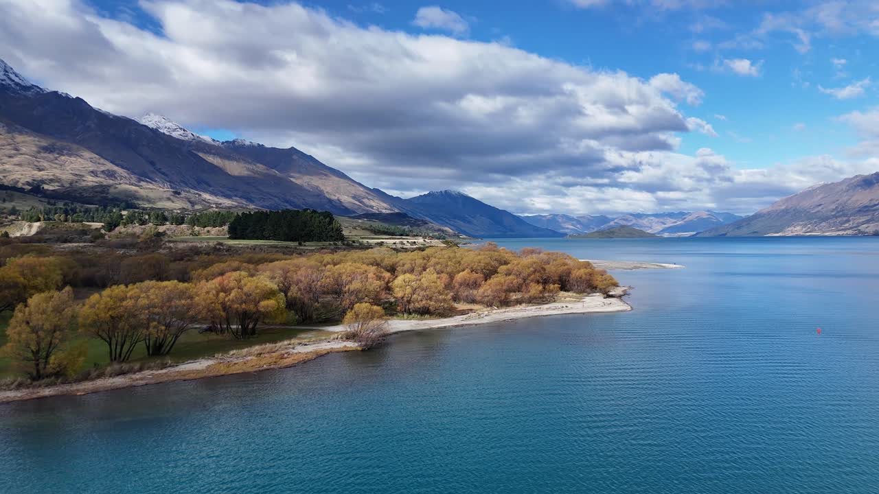 Aerial footage captures Glenorchy's tranquil lake and mountains under vibrant blue skies with dynamic cloud formations