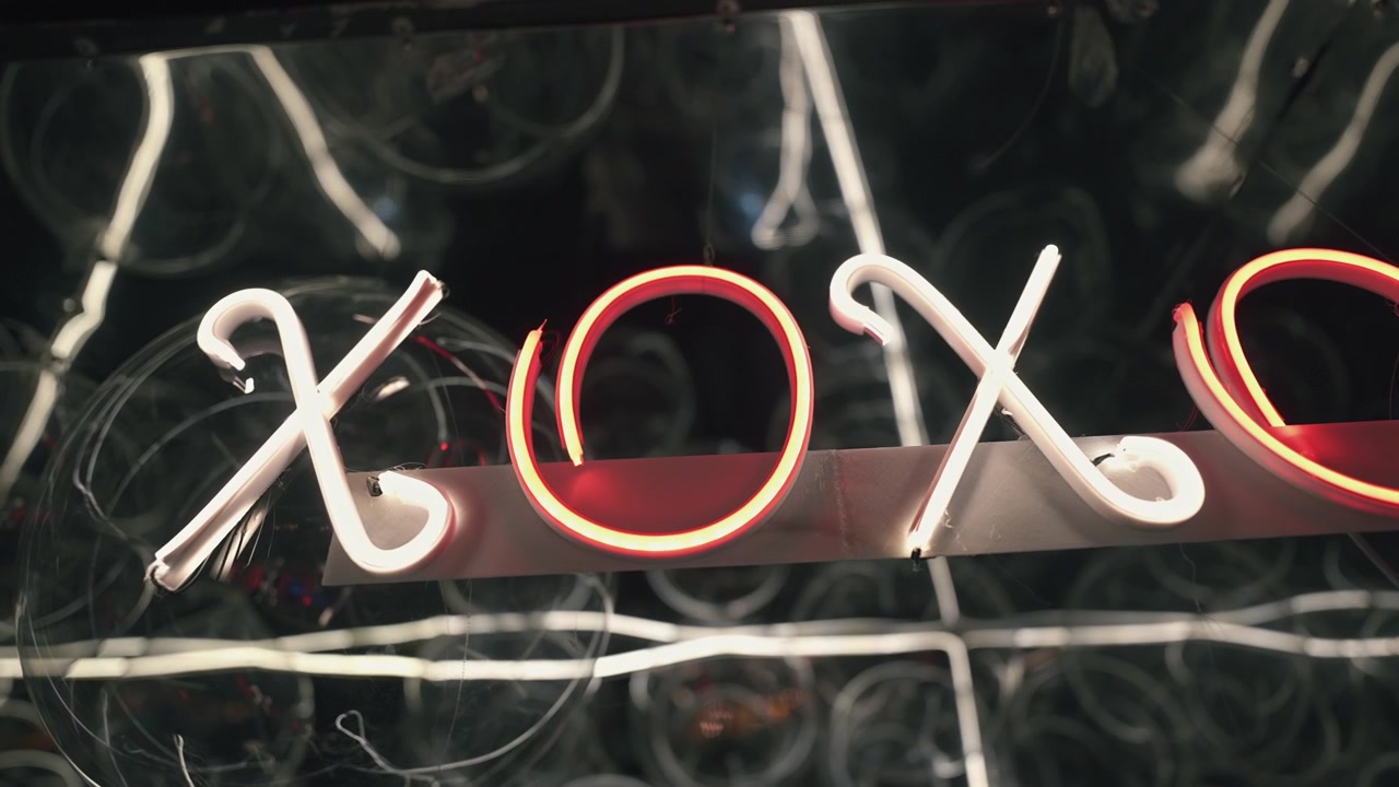 Un'insegna al neon 'XOXO' brilla intensamente su uno sfondo scuro e riflettente. Perfetto per la vita notturna o progetti a tema urbano.