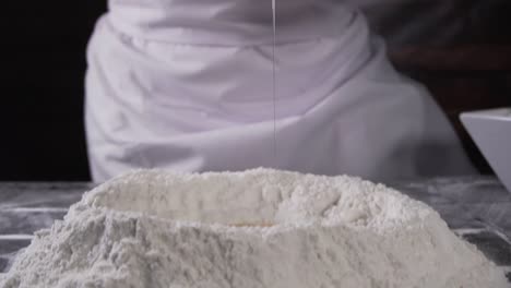 chef cracking and emptying an egg on flour