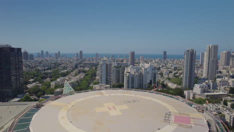 volando sobre la pista de aterrizaje del helicóptero en el techo del edificio de la torre de hospitalización en el centro médico del hospital ichilov de tel aviv, el mar mediterráneo en el fondo - tiro empujado