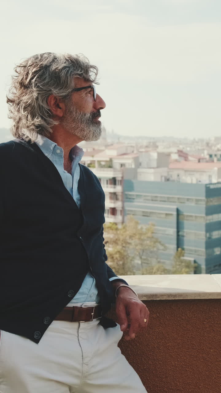 Un uomo di mezza età con i capelli grigi contempla la vista sulla città da un balcone