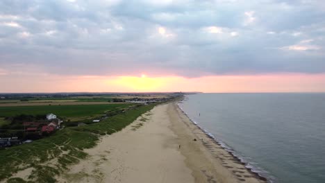 Toma-Aérea-Sobrevolando-Una-Hermosa-Playa-Vacía-Y-Una-Ciudad-Costera-Al-Atardecer