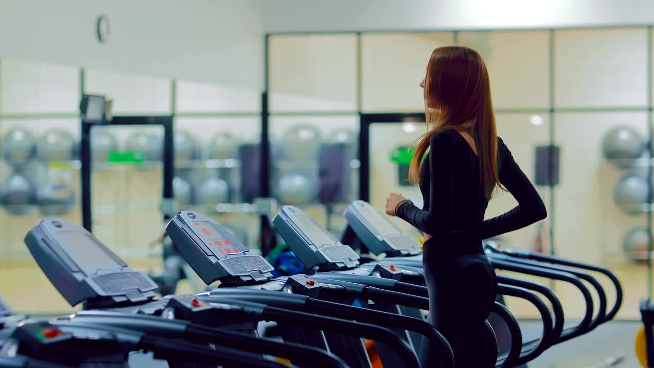 Girl athlete runs on a treadmill, trains in the gym. Slender girl is engaged in fitness in a sports club.