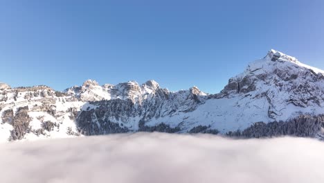 fronalpstock in glarus, switzerland, drone view of snowy peaks towering above tranquil winter clouds, stunning alpine winter landscape.