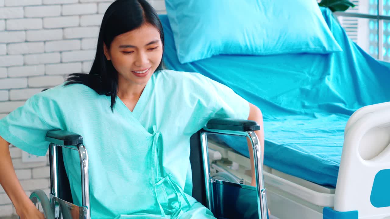 Wanita muda Asia yang ceria di kursi roda di bangsal rumah sakit